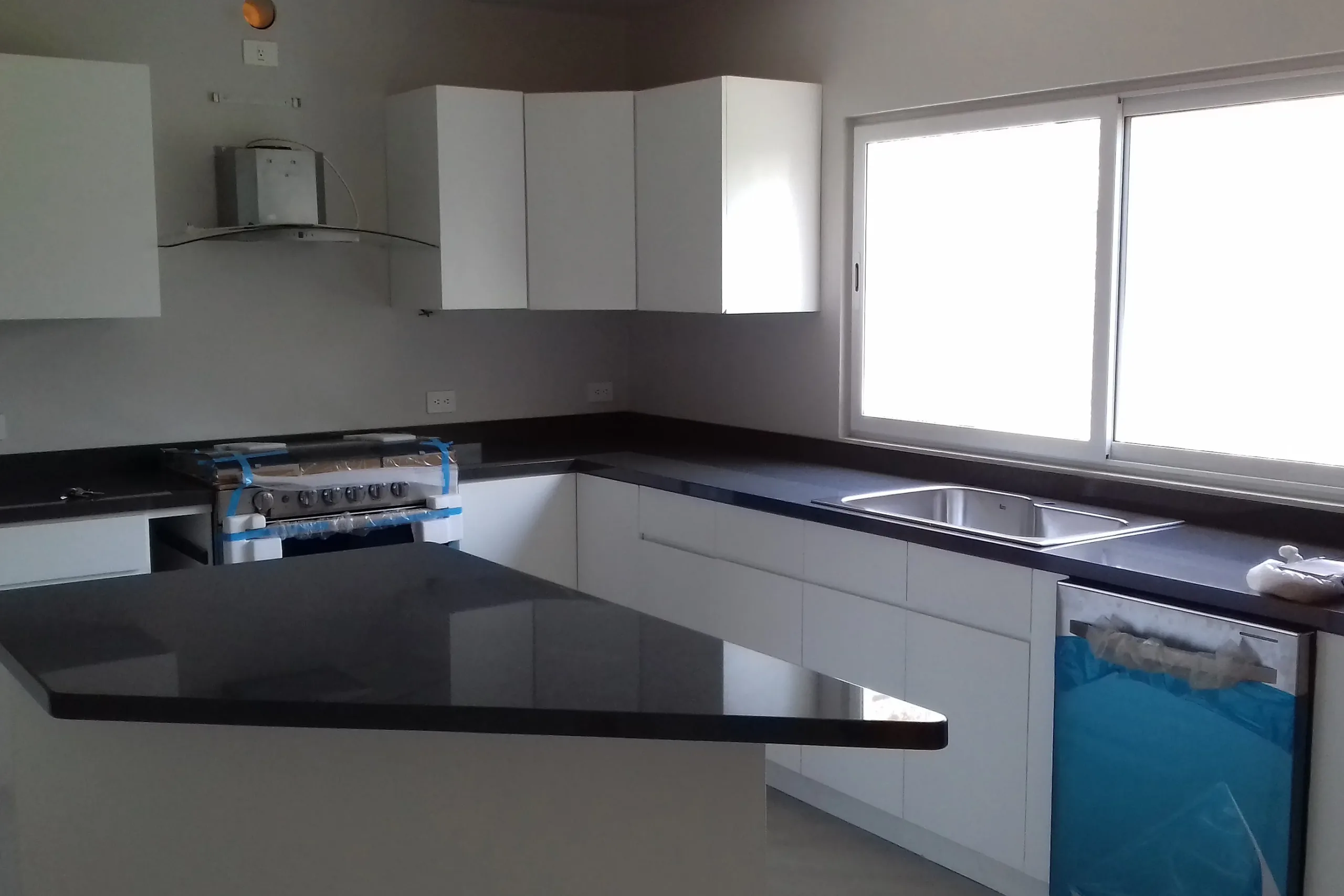 Cocina integral blanca en escuadra con península y cubierta de piedra oscura