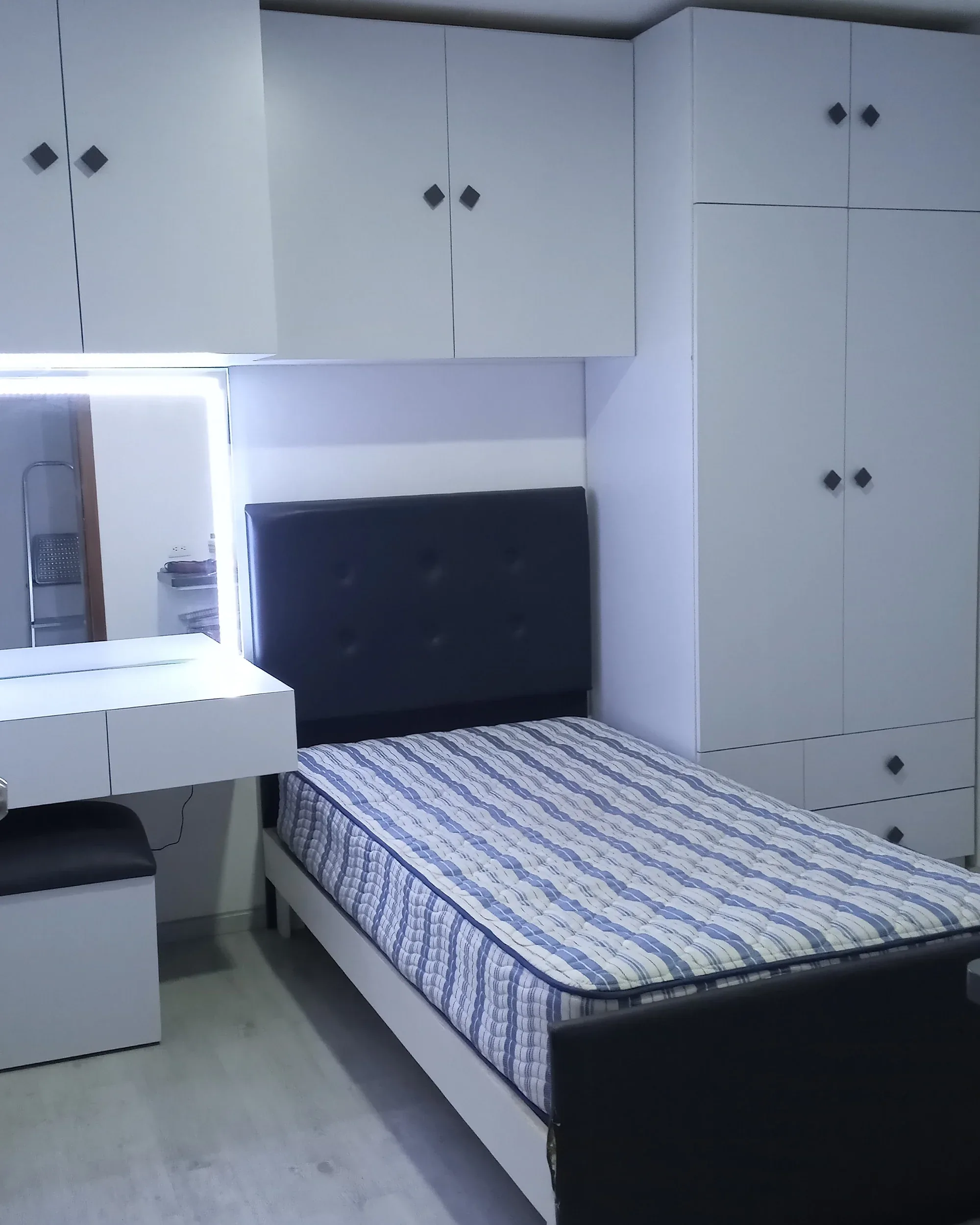 Recámara juvenil con closet blanco de piso a techo, gabinetes altos y tocador con espejo iluminado