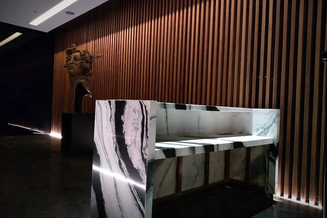 Recepción con barra de piedra veteada y lambrín de listones de madera iluminado
