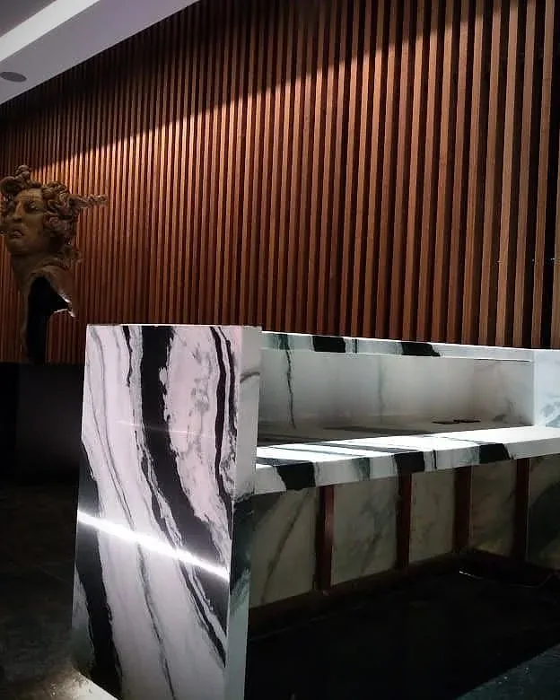 Recepción con barra de piedra veteada y lambrín de listones de madera iluminado