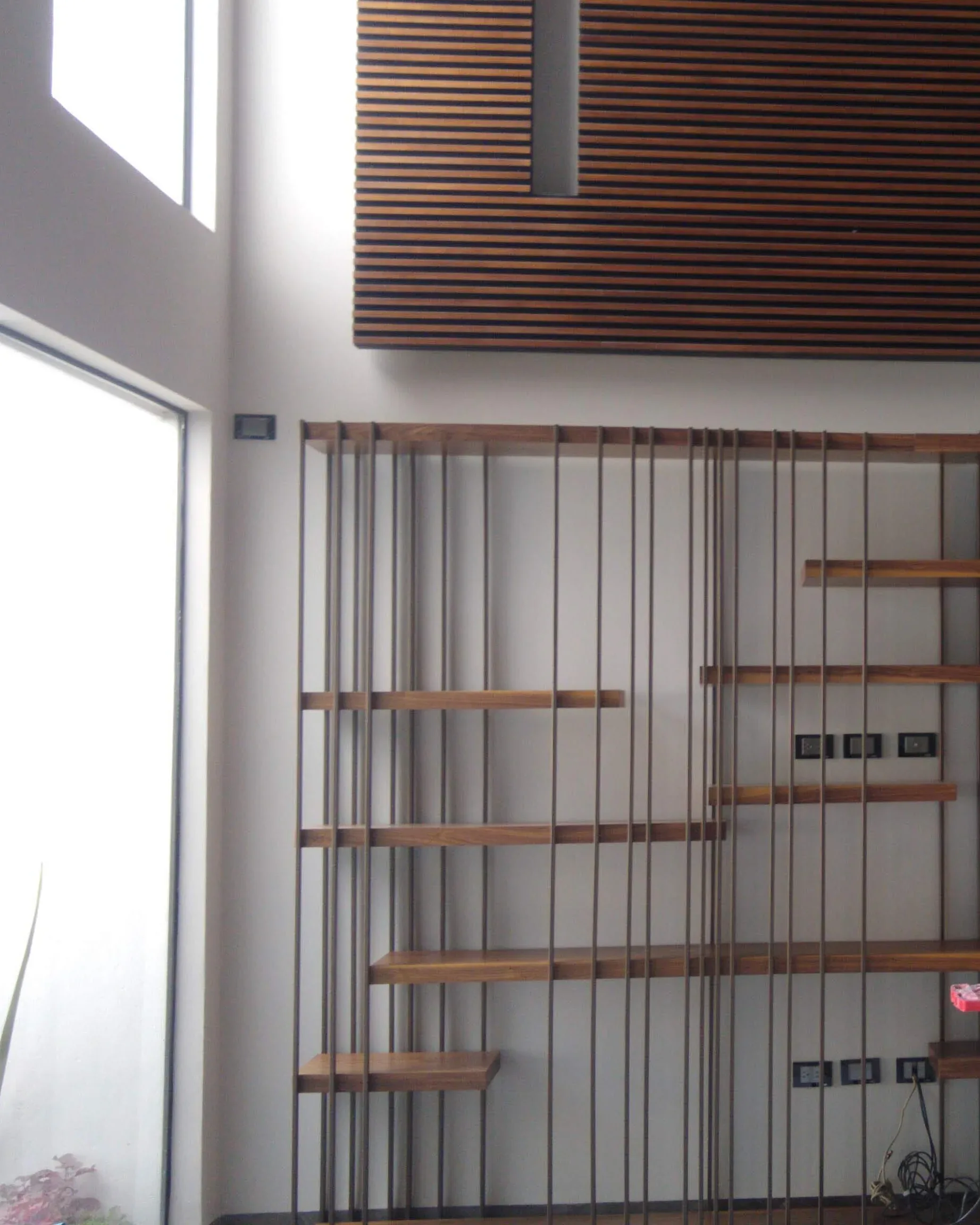 Celosía de varilla de acero con entrepaños de madera en un muro de doble altura